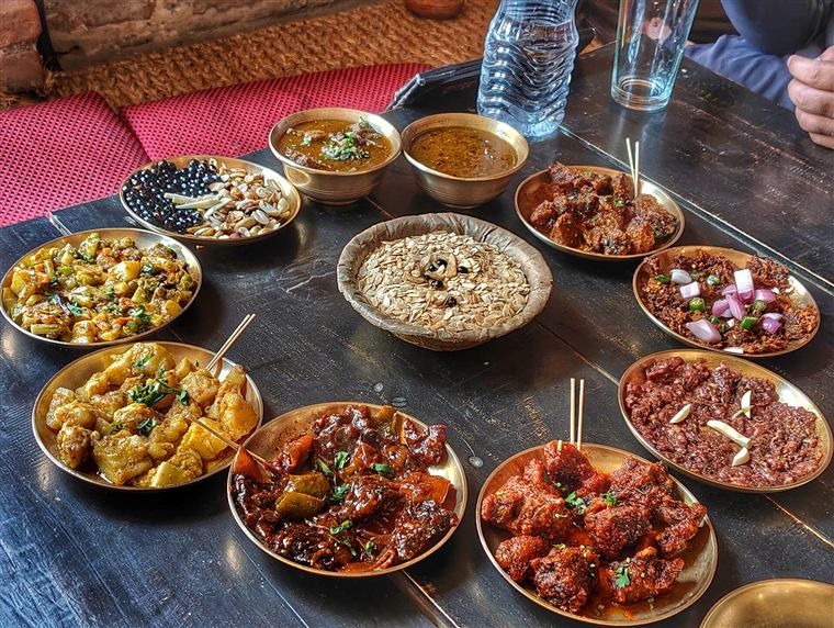Brass bowls of Newari curries and pickles on a dark table